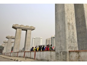 People sit on a ledge between mono rail line pillars under construction in Lagos, Nigeria, on Saturday, Feb. 16, 2019. A last-minute delay of Nigeria's general elections by a week has thrown Africa's biggest democracy into disarray and carries dangers for both President Muhammadu Buhari and his main opponent, Atiku Abubakar. Photographer: George Osodi/Bloomberg