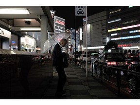 An evening commuter looks at a phone at a taxi stand in Tokyo, Japan, on Friday, Aug. 13, 2021. The spread of the virus in Tokyo is at disaster levels comparable with the heavy rains and flooding hitting Japan's west and residents should stay at home and get vaccinated, Tokyo's governor warned a day after an expert adviser said the virus was out of control.