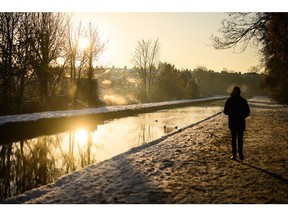 LONDON, ENGLAND - DECEMBER 16: A man walks on the snow-covered path by the New River at sunrise, as steam rises from nearby houses on December 16, 2022 in London, England. Below-zero temperatures have continued across the UK this week. In many parts of the country, snow and ice have prevented travel.