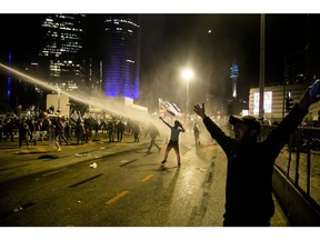 TEL AVIV, ISRAEL - MARCH 27: Israeli protester waves the Israeli flag as police officers use water canon after clashes erupt during a demonstration against the Israeli government's judicial overhaul on March 27, 2023 in Tel Aviv, Israel Gavives Minials' Famissall. Intensified the political crisis sparked by the Netanyahu government's planned judicial overhaul, designed to limit the court's authority over Parliament.