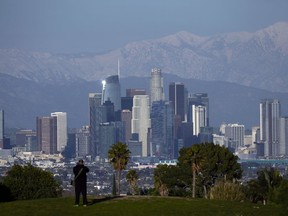 A visitor takes in a view of the city's skyline under the snow-covered San Gabriel mountains after a series of storms Thursday, March 2, 2023, in Los Angeles.