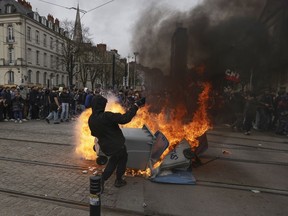 A protester stands next to a burning waste container during a rally in Nantes, western France, Thursday, march 23, 2023. French unions are holding their first mass demonstrations Thursday since President Emmanuel Macron enflamed public anger by forcing a higher retirement age through parliament without a vote.