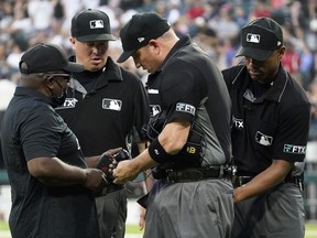 FILE - MLB Network's Kelvin Pickens, left, inspects radio and headset for a call on a play review with umpires Cory Blaser, second from left, Edwin Moscoso, right, and Dan Bellino after the first inning of a baseball game in Chicago, Friday, July 22, 2022. Major League Baseball struck a deal with Zoom Video Communications Inc. allowing on-field umpires to watch videos being evaluated by the replay operations center during contested calls. On-field umps this year will have 12.9-inch iPad Pro tablets brought out to them by a technician.