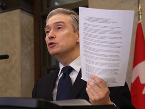 Innovation, Science and Industry Minister Francois-Philippe Champagne holds up a contract between the telecoms and the federal government as he speaks at a news conference about the Rogers-Shaw merger on Parliament Hill in Ottawa on Friday, March 31, 2023.