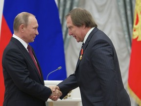 FILE - Russian President Vladimir Putin, left, presents a medal to Russian cellist Sergei Roldugin, during an awarding ceremony in Moscow's Kremlin, Russia, on Thursday, Sept. 22, 2016. Four former bankers with the now-shuttered Swiss affiliate of a major Russian bank have gone on trial over allegations that they didn't properly check accounts opened in the name of a Russian cellist with longtime ties to President Vladimir Putin.