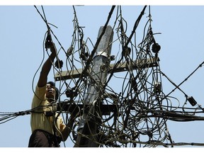 A municipal electricity supply worker uses his pliers to untangle power lines atop a pole in downtown Yangon, Myanmar April 21, 2004. Photographer: UDO WEITZ/BLOOMBERG