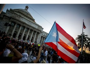 A demonstrator waves a Puerto Rican flag outside the Capitol building during a protest against the government in San Juan, Puerto Rico, on Monday, Jan. 20, 2020. People in a southern Puerto Rico city discovered a warehouse filled with unused emergency supplies, then set off a social media uproar Saturday when they broke in to retrieve goods as the area struggles to recover from a strong earthquake, the Associated Press reported.