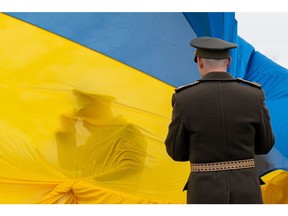 Ukrainian military personnel hold a Ukrainian national flag during an event to mark the anniversary of the city's de-occupation in Bucha.