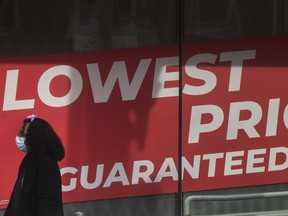 A pedestrian walks past a store's signage stating "Lowest Price Guranteed" on Parliament Street in Toronto.