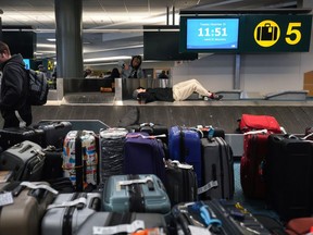 People rest on a baggage carousel as luggage lines the floor at Vancouver International Airport in Richmond, B.C., on Tuesday, December 20, 2022. Some critics have suggested that recent problems with flight delays and cancellations in Canada is further proof that this country's competition framework is broken.