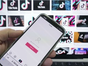 A sign up page for the application TikTok is shown on a cell phone in front of a screen with logos for the company in Sydney, Tuesday, April 4, 2023. Australia had become the last of the Five Eyes security partners to ban the Chinese-owned TikTok ap from government devices.