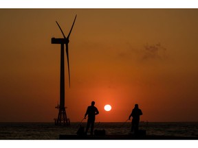 People fish in front of a wind turbine as sun sets in the background in Jeju, South Korea, on Wednesday, June 14, 2017. Photographer: SeongJoon Cho/Bloomberg