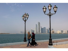 A couple walk along the Corniche backdropped by commercial and residential skyscrapers in Abu Dhabi, United Arab Emirates, on Sunday, April 10, 2022. Abu Dhabi regulators approved a framework for special purpose acquisition companies, looking to capture some of the blank-check boom that has gripped global markets for the past two years. Photographer: Christopher Pike/Bloomberg