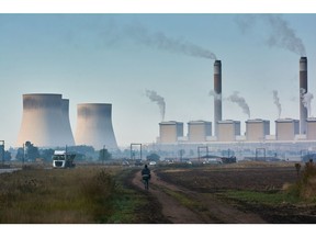 A pedestrian walks through a field, backdropped by the Eskom Holdings SOC Ltd. Kendal coal-fired power station in Mpumalanga, South Africa, on Friday, May 5, 2023. Debt-strapped Eskom is currently implementing daily blackouts because its dilapidated power plants are unable to supply enough electricity to meet demand and it doesn't have the money to invest in capital equipment.