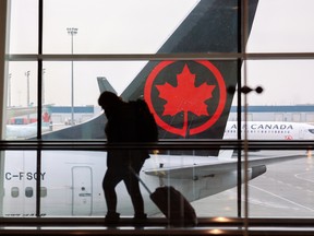 Travellers move between gates at the Calgary International Airport with an Air Canada plane in the background.