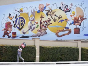 A picketer walks underneath a billboard highlighting Warner Bros. animated characters during a Writers Guild rally, Monday, May 22, 2023, outside Warner Bros. Studios in Burbank, Calif.