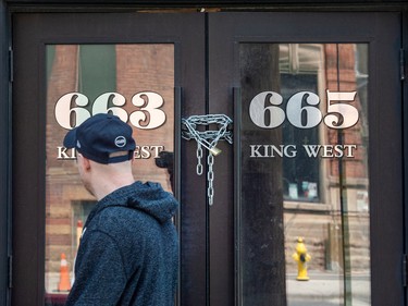 A pedestrian looks upon the locked doors of a shuttered bar on Toronto's King Street West.