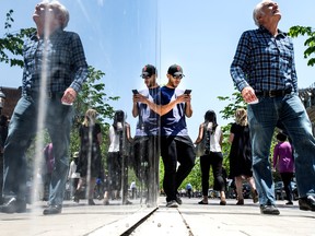 A young man with a cellphone is mirrored with other pedestrians in Toronto