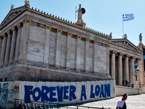 A person walks past a graffiti refering to the Greek debt and reading "Forever a loan" outside the Academy of Athens building