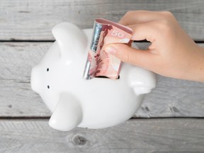 Hand of a young person putting Canadian money in a piggy bank