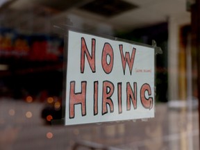 A now hiring sign tacked to a store window