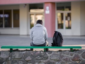 A teen sitting on a bench outside a school.