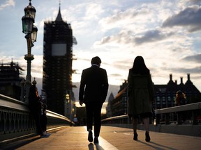 A couple walk across Westminster Bridge as the sun sets beside the Palace of Westminster.