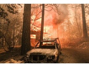 A structure burns behind a charred vehicle on Jerseydale road during the Oak Fire in Mariposa County, California, US, on Saturday, July 23, 2022. A fast-moving wildfire near Yosemite National Park exploded in size Saturday into one of California's largest wildfires of the year, prompting evacuation orders for thousands of people and shutting off power to more than 2,000 homes and businesses.