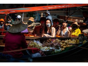 Tourists ride past a vendor at a floating market in Damnoen Saduak, Thailand. Photographer: Eduardo Leal/Bloomberg