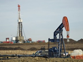 A pumpjack works in the foreground with a drilling rig in the back.