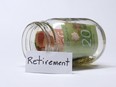 A glass jar resting on its side with Canadian money inside, and the word retirement on a card propped up on the outside