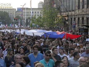 People hoist a Serbian flag as they walk down a street during an anti-government protest in Belgrade, Serbia, Saturday, June 3, 2023. Tens of thousands of people rallied in Serbia's capital on Saturday in protest of the government's handling of a crisis after two mass shootings in the Balkan country.