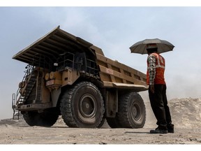 A mining worker under an umbrella shelters from the sun as a dump truck passes at the coal mine, operated by South Eastern Coalfields Ltd., in Gevra, Chhattisgarh, India, on Wednesday, May 10, 2023. India has to keep its power grid standing to cope with brutal temperatures, digging up expanding quantities of the dirtiest fossil fuel. Photographer: Anindito Mukherjee/Bloomberg