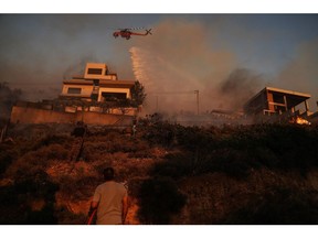An S-64E Erickson Air-Crane of the Greek fire brigade drops water to extinguish a burning field during a wildfire in Saronida, south of Athens, Greece, on Monday, July 17, 2023. A fire near Athens is threatening homes, as strong winds and high temperatures fuel the blaze.