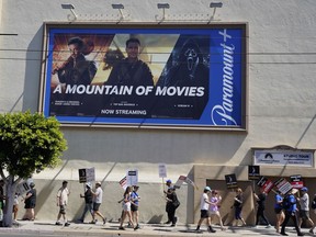 An advertisement for streaming service Paramount+ appears above striking writers and actors at rally outside Paramount studios in Los Angeles on Friday, July 14, 2023. This marks the first day actors formally joined the picket lines, more than two months after screenwriters began striking in their bid to get better pay and working conditions.