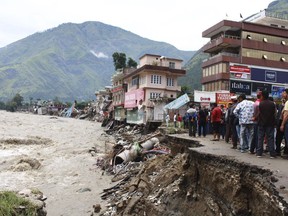 People stand by a road washed away by the River Beas swollen due to heavy rains in Kullu District, Himachal Pradesh, India, Tuesday, July 11, 2023. Heavy monsoon rains caused landslides and flash floods in the country's north, killing at least 15 people over the past few days.