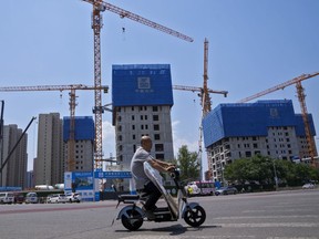 FILE - A man rides on an electric bike past by a residential buildings under construction in Beijing on June 5, 2023. Chinese factory activity contracted in July as export orders shrank, a survey showed Monday, adding to pressure on the ruling Communist Party to reverse an economic slowdown.