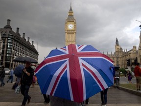 A pedestrian shelters from the rain beneath a Union flag themed umbrella as they walk near the Big Ben clock face and the Elizabeth Tower at the Houses of Parliament in central London.