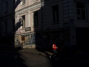 A woman walks past a building lit by a shaft of light in Kyiv, Ukraine, Tuesday, July 4, 2023.