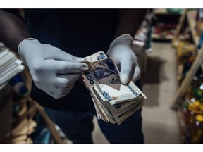 A vendor wearing protective latex gloves counts out Nigerian naira banknotes in a store in Lugbe district in Abuja, Nigeria, on Wednesday, June 3, 2020. The government of Nigeria, whose revenue could be slashed by more than half this year due to the oil-price slump, finalized plans for a revised budget that keeps spending almost intact, and that will mean more borrowing.