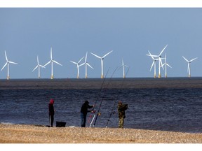 Offshore wind turbines beyond fishermen on the beach at the Scroby Sands Wind Farm, operated by E.ON SE, near Great Yarmouth, UK, on Friday, May 13, 2022. The U.K. will introduce new laws for energy to enable a fast build out of renewables and nuclear power stations as set out in the government's energy security strategy last month.