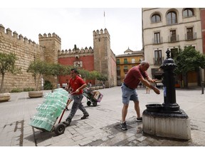 A worker delivers bottled water as a pedestrian cools himself at a public fountain during a heat wave in Seville, Spain, on Wednesday, June 15. 2022. The scorching weather provides another example of the impact climate change will have as countries' reliance on burning fossil fuels makes the planet hotter.