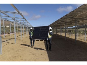 Workers carry a solar panel for installation at the Karoo Fresh Produce (Pty) Ltd. farm in Groenfontein, South Africa, on Wednesday, Aug. 24, 2022. Sun Exchange invites investors to buy solar cells at a project of their choice, where the solar energy customers pay a fee for use, with part of that paid back to investors in either South African rand or Bitcoin.