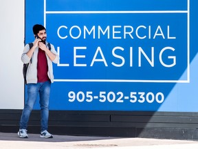A person talks on a phone standing beside a sign advertising commercial real estate for lease in Toronto.