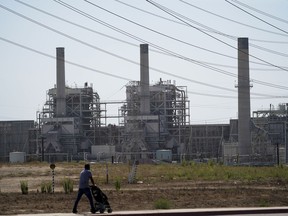 FILE - A man pushes a stroller near the AES power plant in Redondo Beach, Calif., Sept. 7, 2022. The California Energy Commission voted Wednesday, Aug. 9, 2023, to extend the life of three gas power plants along the state's southern coast through 2026, postponing a shutoff deadline previously set for the end of this year. The vote would keep the decades-old facilities -- Ormond Beach Generating Station, AES Alamitos and AES Huntington Beach -- open so they can run during emergencies.