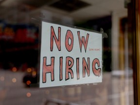 A 'now hiring' sign posted on the window of a business looking to hire workers.