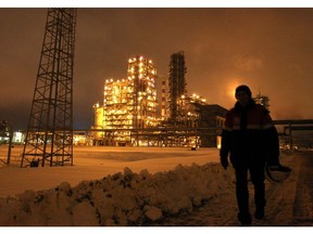 An employee carries a safety helmet through the snow at the illuminated Lukoil-Nizhegorodnefteorgsintez petroleum refinery, operated by OAO Lukoil, in Nizhny Novgorod, Russia.