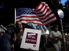 A man carries the U.S. flag with a placard reading, "horror movie for the sake of reasonableness," as Israelis march in support of the judicial system during a protest against the plans by Prime Minister Benjamin Netanyahu's government to overhaul it, in Tel Aviv, Israel, Wednesday, Aug. 2, 2023.