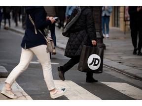 A shopper carries a JD Sports Fashion Plc bag in Paris, France, on Tuesday, May 9, 2023. JD Sports is in exclusive talks to buy French chain Courir France SAS for an enterprise value of €520 million ($570 million) as it further expands in continental Europe, heightening its rivalry with Frasers Group Plc. Photographer: Benjamin Girette/Bloomberg