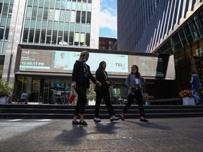 Pedestrians walk past a TSX sign board in Toronto's financial district. Some Canadians have put investing plans on ice amid economic uncertainty, a survey says.